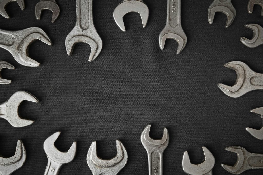 A collection of metal open-ended wrenches arranged in a circular pattern on a black fabric background, leaving a clear empty space in the center. Each wrench represents a tool with a specific shape and function, just like email platforms, each is designed to solve particular problems.