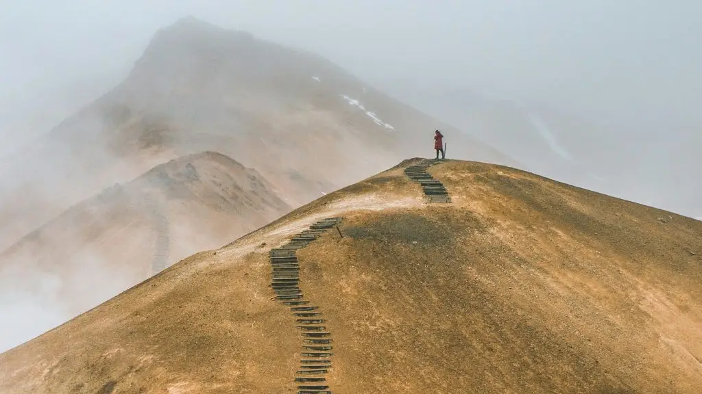 Wooden steps winding up a foggy mountain ridge toward a person standing at the summit.